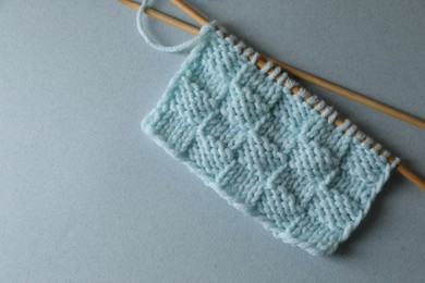 Photo of Soft turquoise knitting and needles on light blue background, top view. Space for text