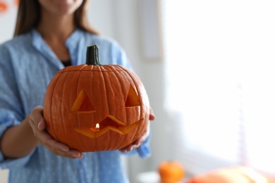 Photo of Woman holding pumpkin jack o'lantern indoors, closeup with space for text. Halloween celebration