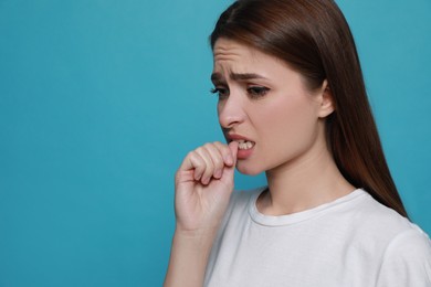 Young woman biting her nails on light blue background. Space for text