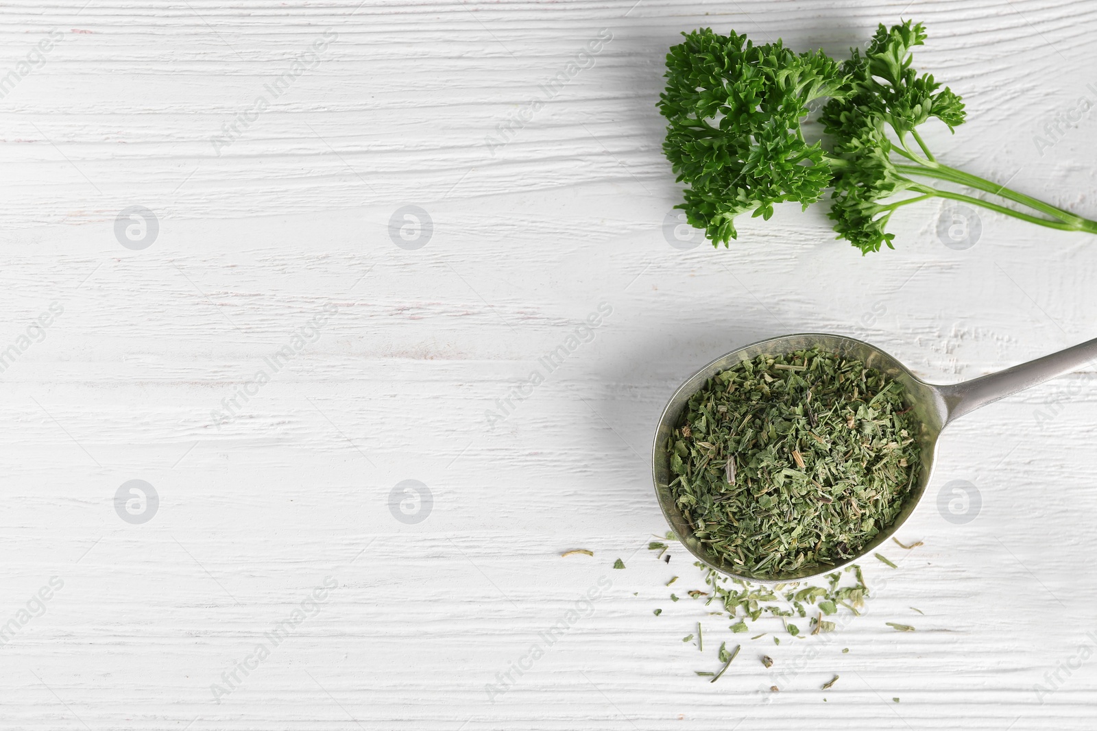 Photo of Spoon with dry parsley and space for text on white wooden background, top view