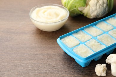 Photo of Cauliflower puree in ice cube tray and fresh cauliflower on wooden table. Space for text