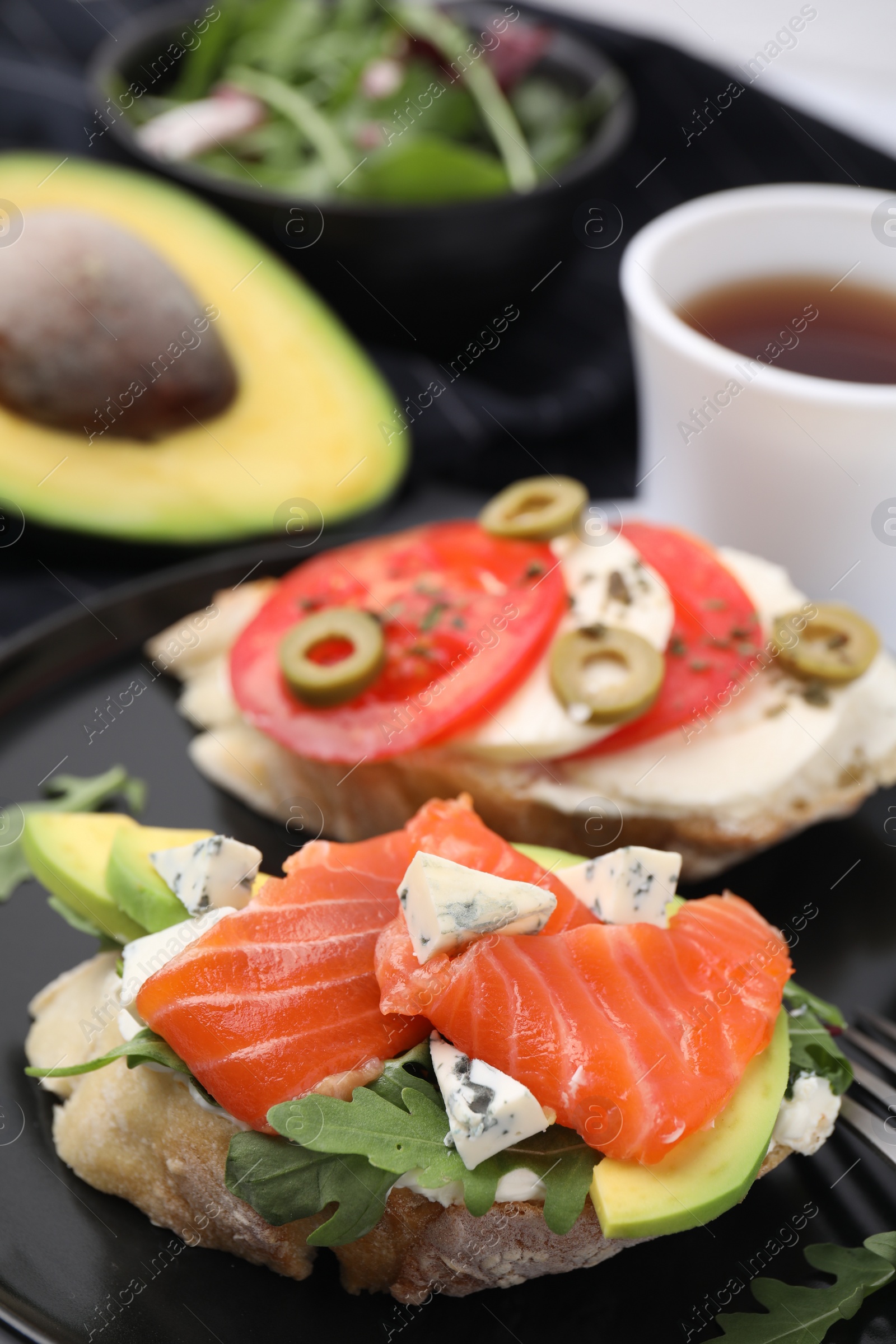 Photo of Different tasty bruschettas on black plate, closeup