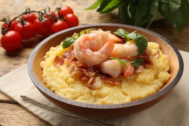 Fresh tasty shrimps, bacon, grits and basil in bowl on wooden table, closeup