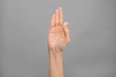 Woman showing F letter on grey background, closeup. Sign language
