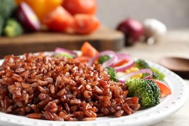 Photo of Plate of boiled brown rice with vegetables on table, closeup