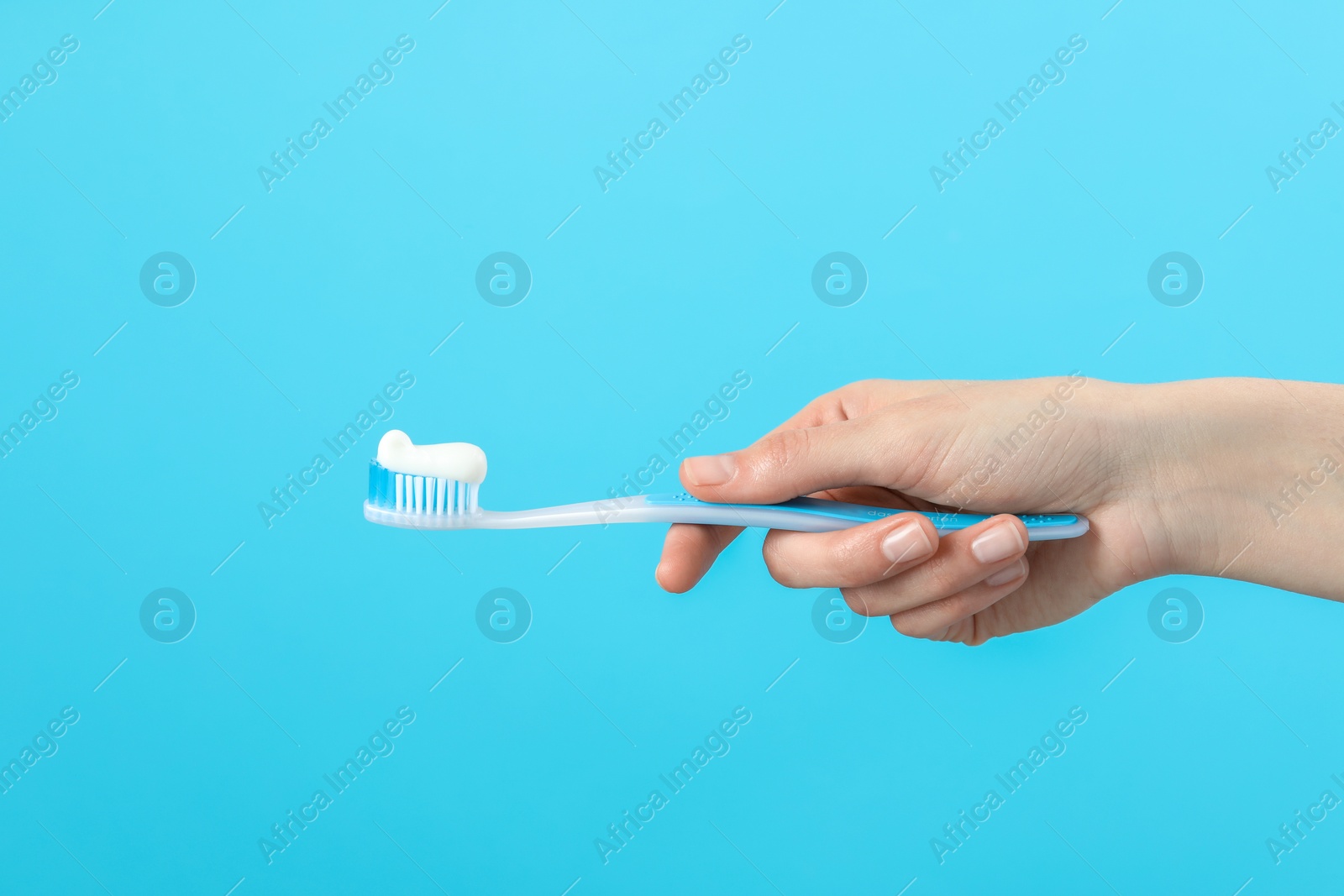 Photo of Woman holding toothbrush with paste on light blue background, closeup