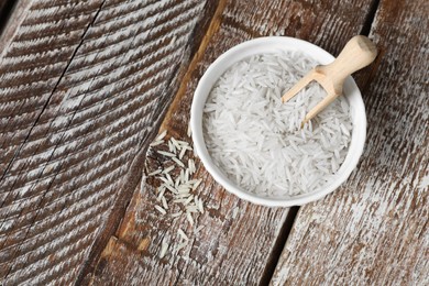 Photo of Raw basmati rice in bowl and scoop on wooden table, top view. Space for text