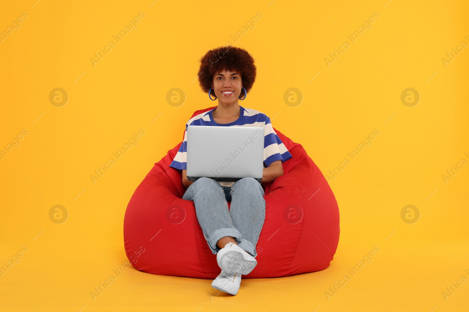 Photo of Beautiful young woman with laptop sitting on beanbag chair against orange background