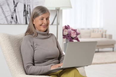 Photo of Beautiful senior woman using laptop in armchair at home