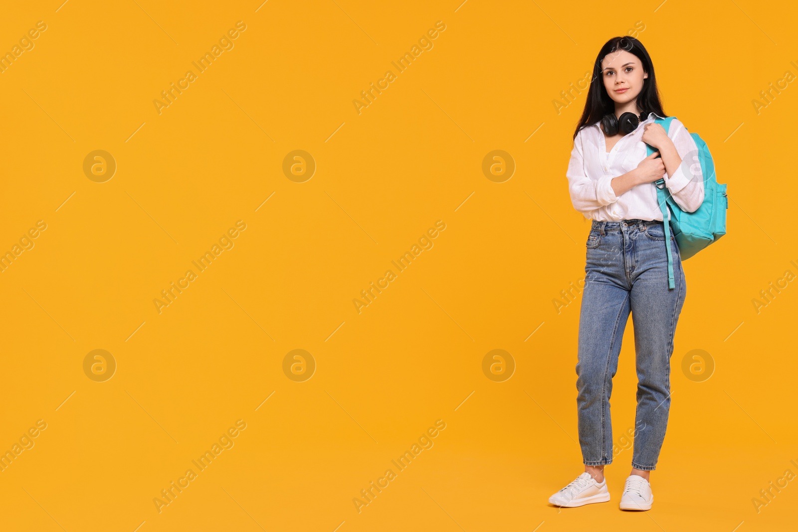 Photo of Student with backpack and headphones on yellow background. Space for text