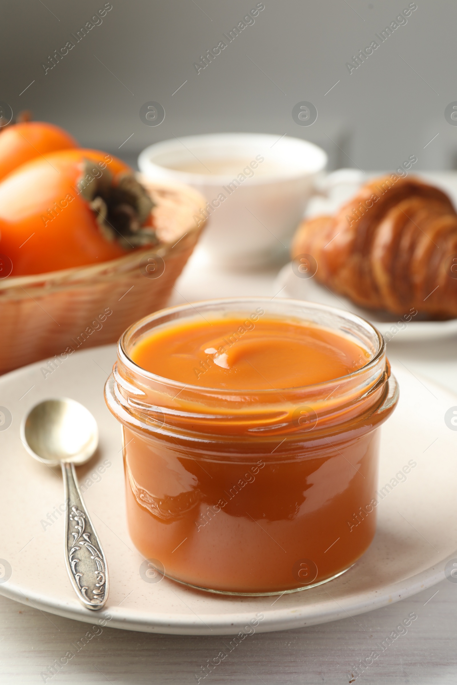 Photo of Delicious persimmon jam in glass jar served on white wooden table