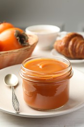 Photo of Delicious persimmon jam in glass jar served on white wooden table