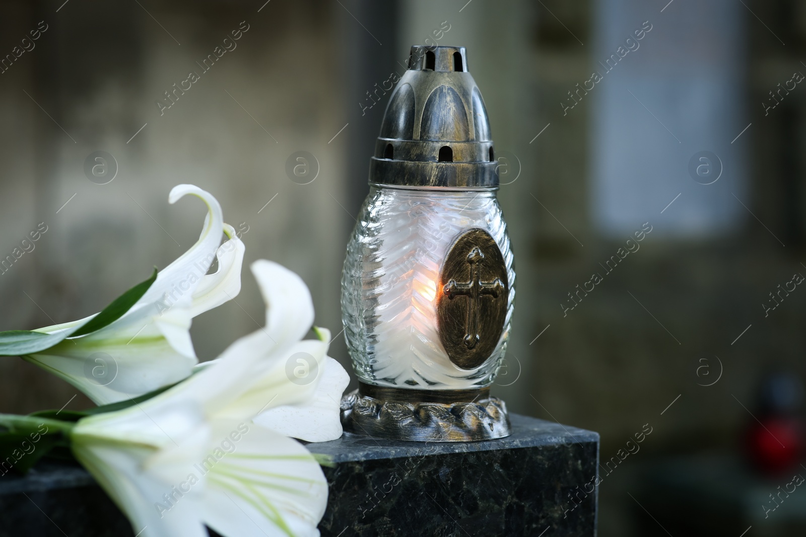 Photo of Lilies and grave lantern with burning candle on tombstone in cemetery, space for text