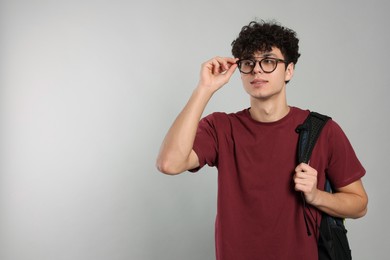 Handsome young man with backpack on light grey background. Space for text