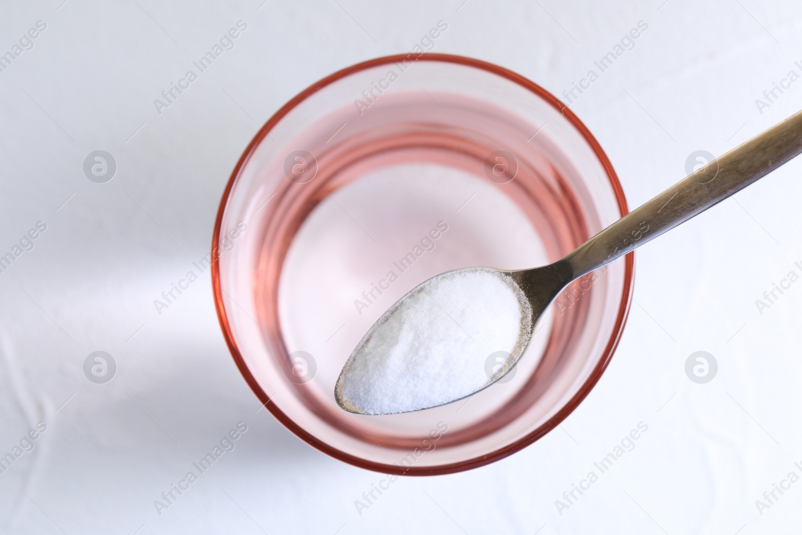 Photo of Spoon with baking soda over glass of water on white background, top view