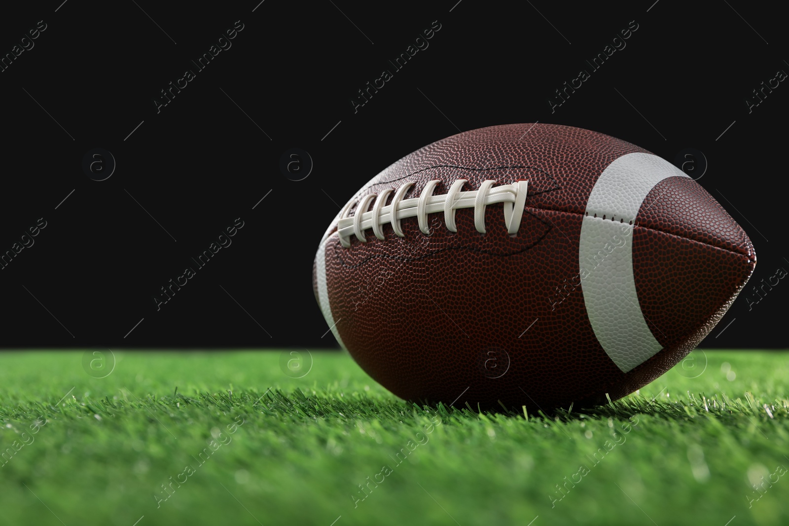 Photo of Rugby ball on green grass against black background, space for text