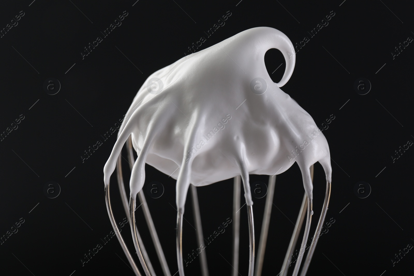 Photo of Whisk with whipped cream on black background, closeup