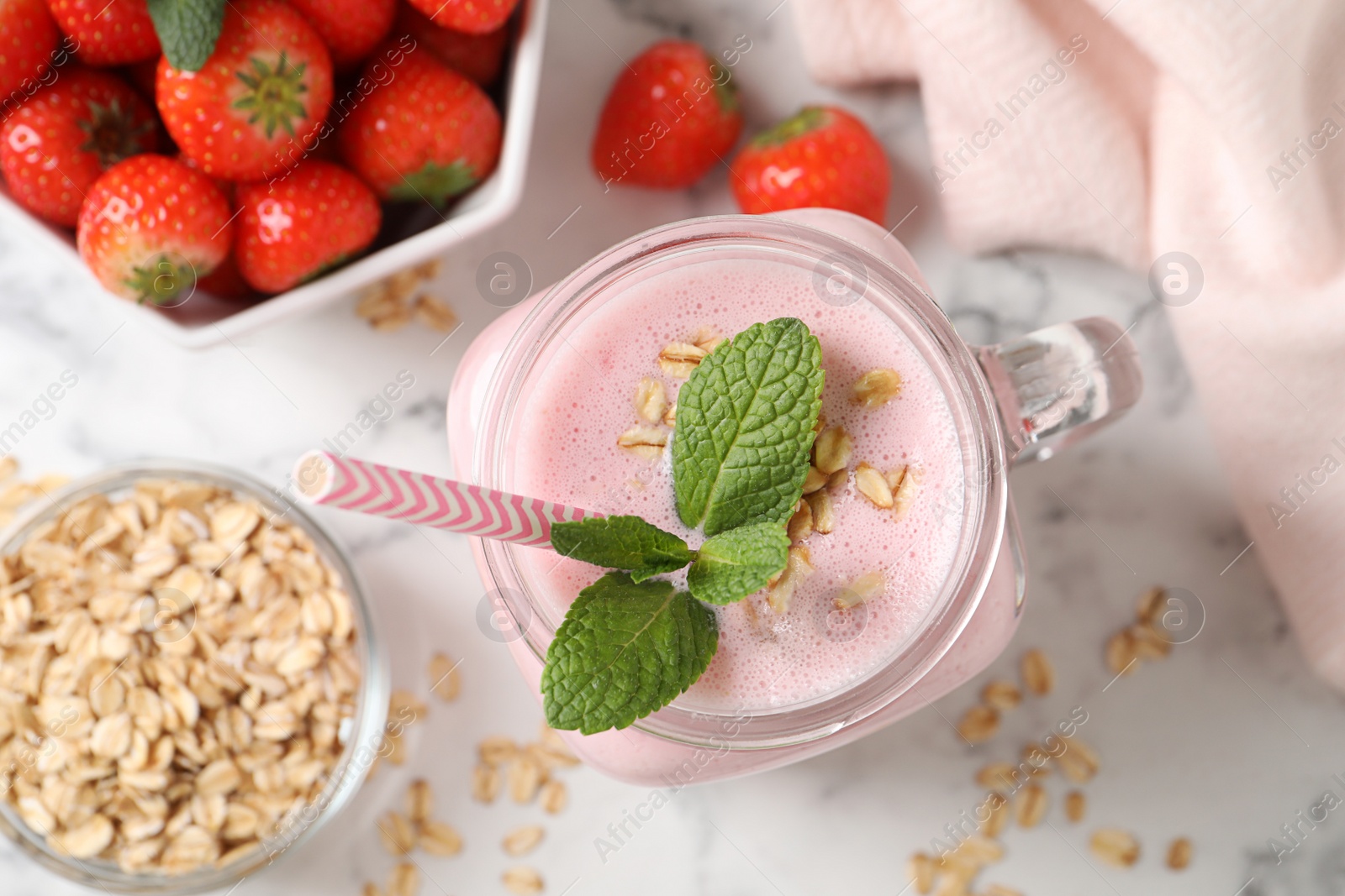 Photo of Mason jar of tasty strawberry smoothie with oatmeal and mint on white marble table, flat lay