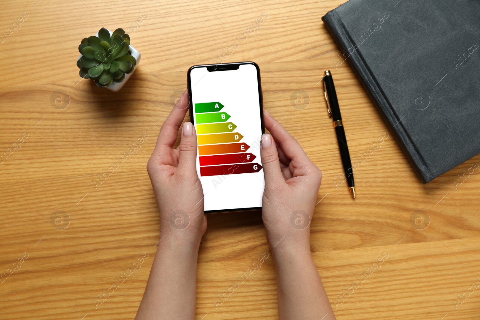 Image of Energy efficiency. Woman using smartphone with colorful rating on display at wooden table, top view