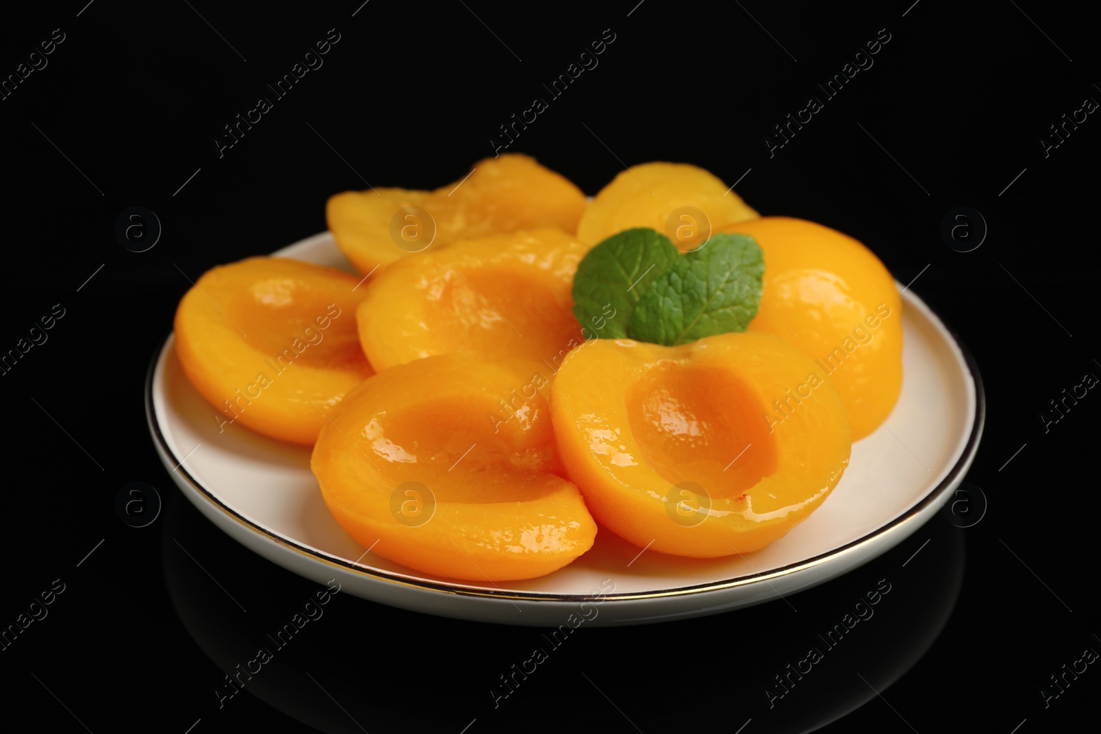 Photo of Plate with canned peach halves on black background