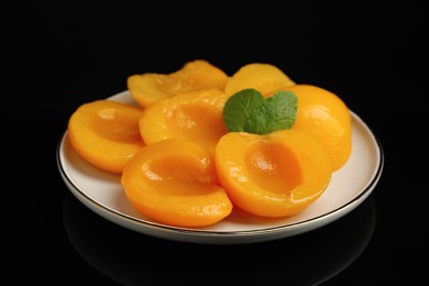 Plate with canned peach halves on black background