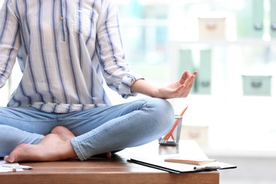 Photo of Woman meditating on table in office during break, closeup with space for text. Zen yoga