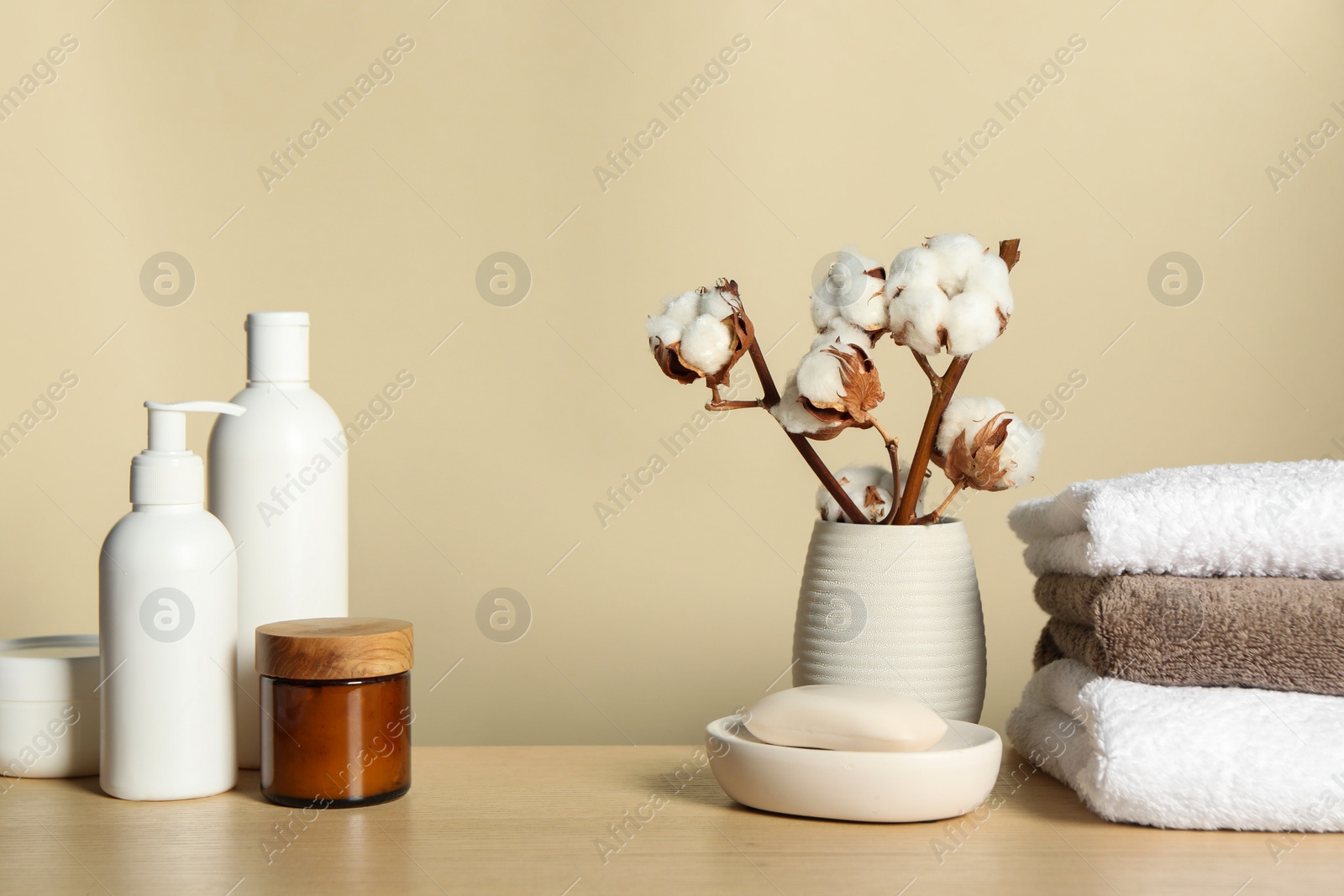 Photo of Different bath accessories and cotton flower on wooden table against beige background