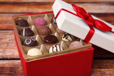 Photo of Red box with tasty chocolate candies on wooden table, closeup