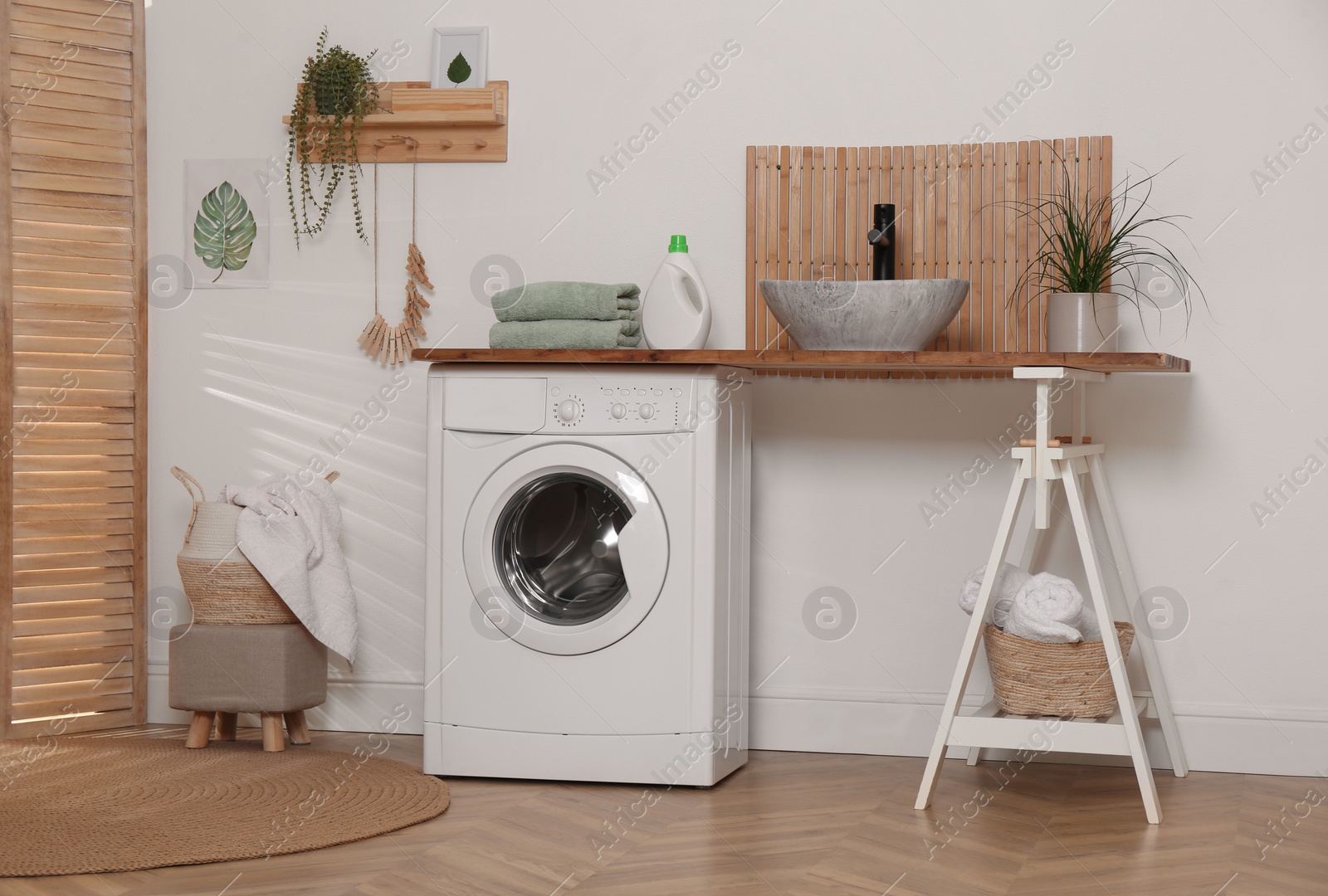 Photo of Laundry room interior with modern washing machine and stylish vessel sink on wooden countertop