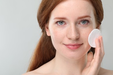 Beautiful woman with freckles wiping face on grey background, closeup. Space for text