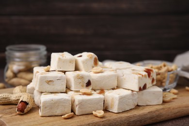 Photo of Pieces of delicious nougat and nuts on wooden board, closeup