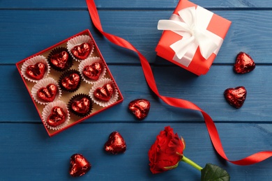 Heart shaped chocolate candies, gift box and ribbon on blue wooden table, flat lay