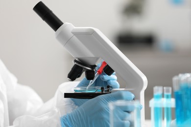 Scientist dripping sample onto Petri dish while working with microscope in laboratory, closeup