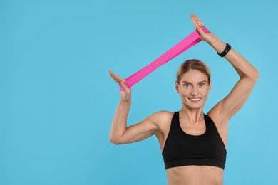 Woman exercising with elastic resistance band on light blue background. Space for text
