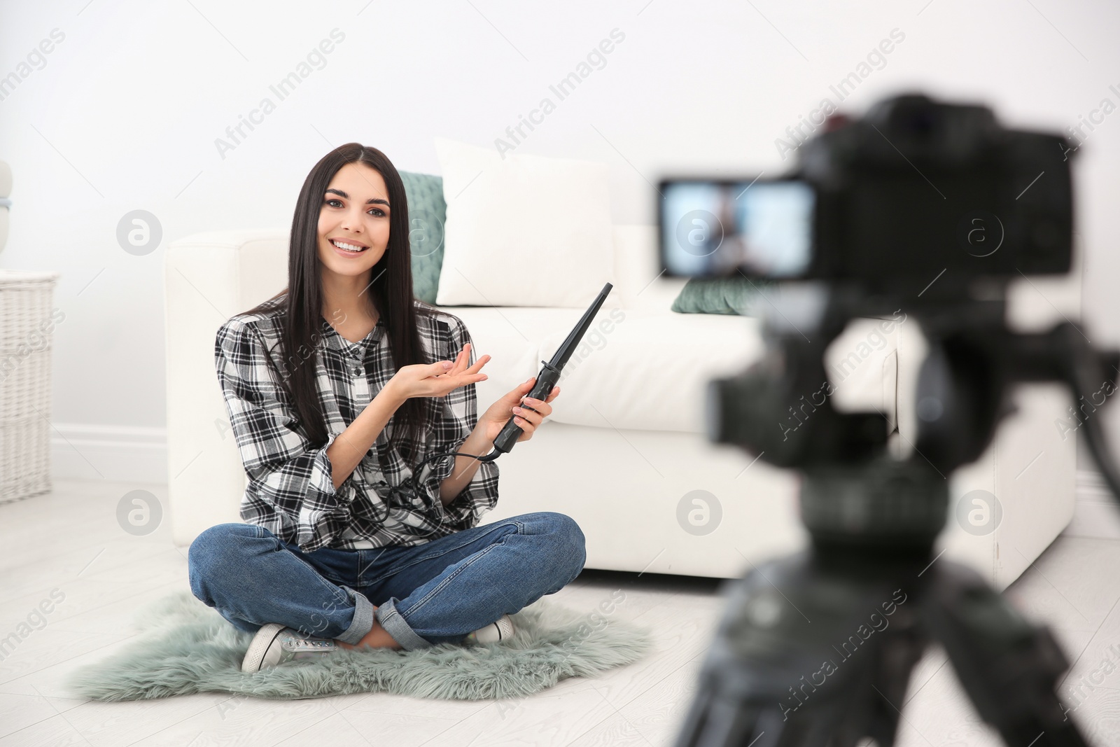 Photo of Young blogger with hair curler recording video on camera at home