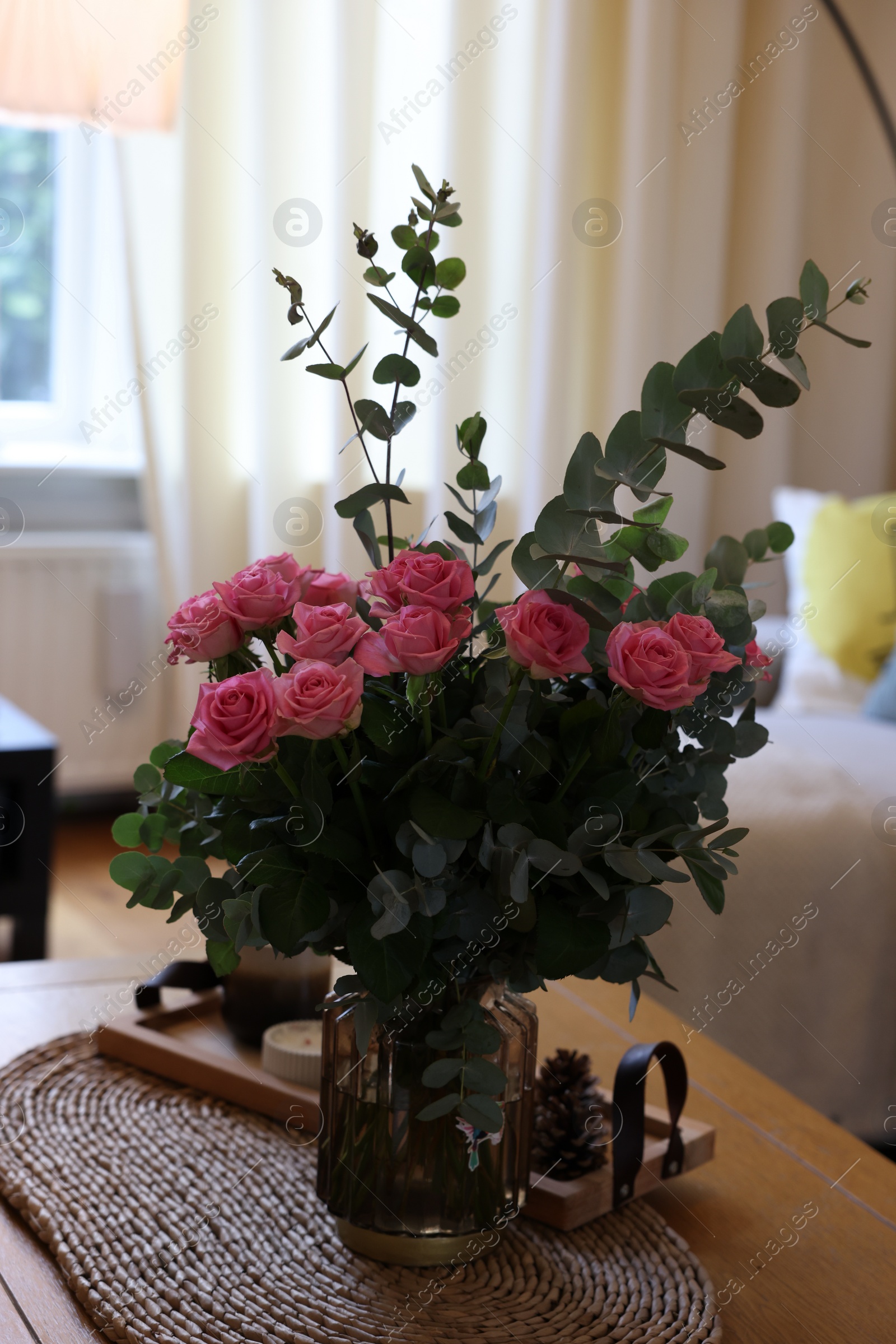 Photo of Beautiful bouquet of roses and eucalyptus branches in vase near candles on table at home