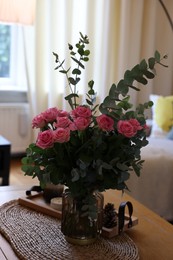 Photo of Beautiful bouquet of roses and eucalyptus branches in vase near candles on table at home