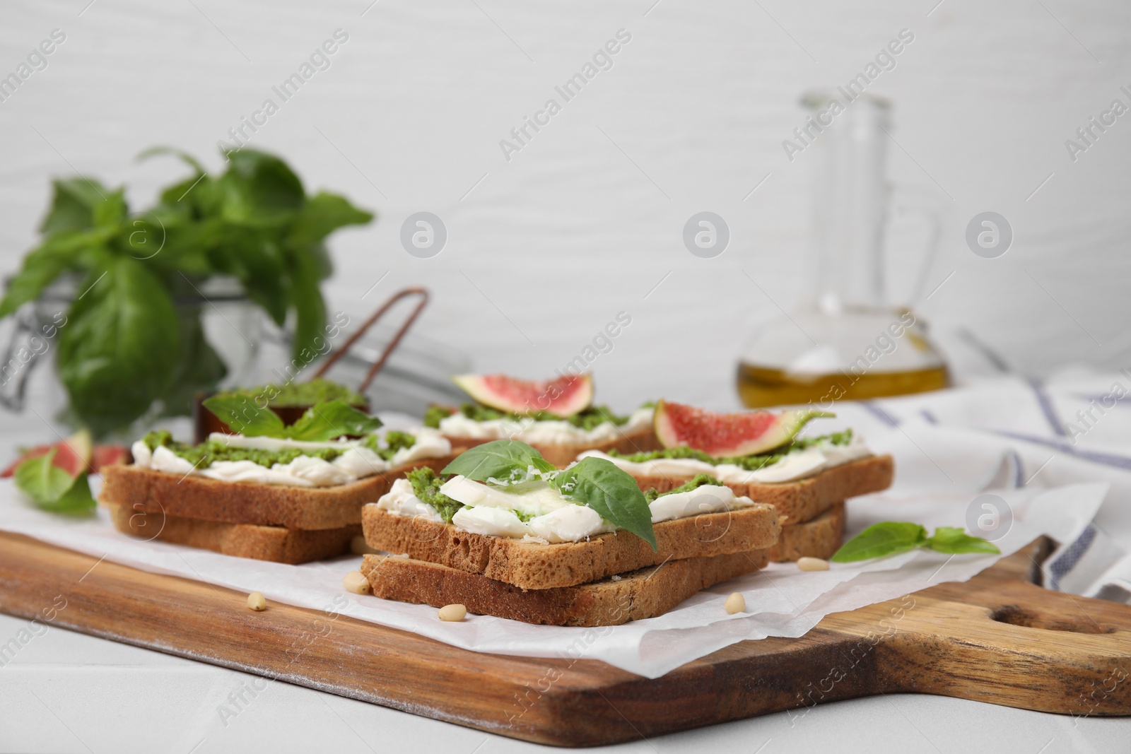 Photo of Tasty bruschetta with cream cheese, pesto sauce and fresh basil on wooden board