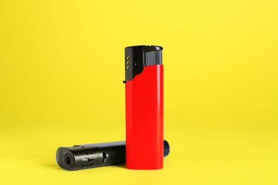 Stylish small pocket lighters on yellow background