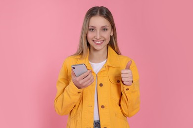 Photo of Teenage girl with smartphone showing thumb up on pink background