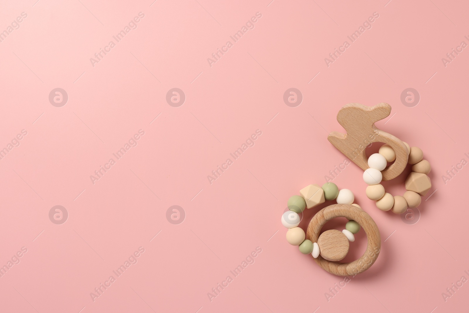 Photo of Baby accessories. Wooden rattles on pink background, flat lay. Space for text