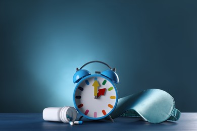 Photo of Alarm clock, soporific pills and sleeping mask on wooden table, space for text. Insomnia treatment