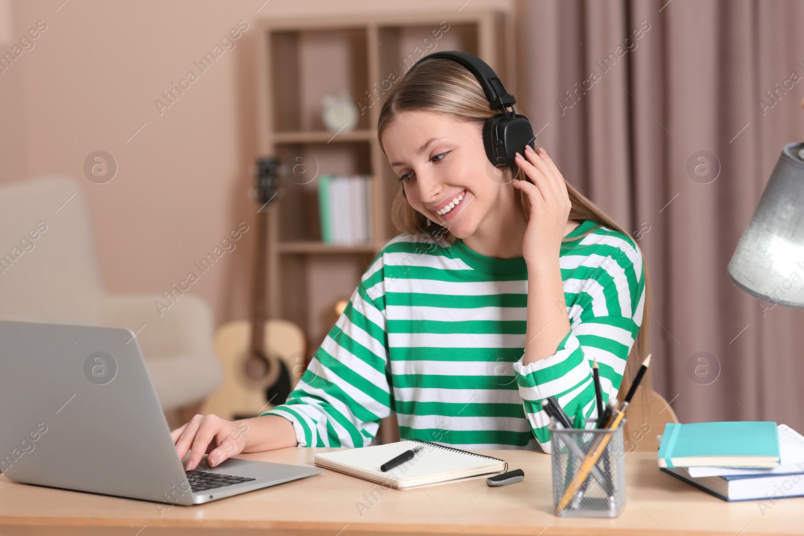 Photo of Online learning. Smiling teenage girl typing on laptop at home