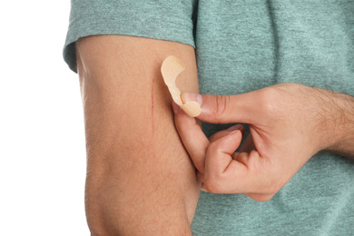 Photo of Man putting sticking plaster onto arm against on background, closeup