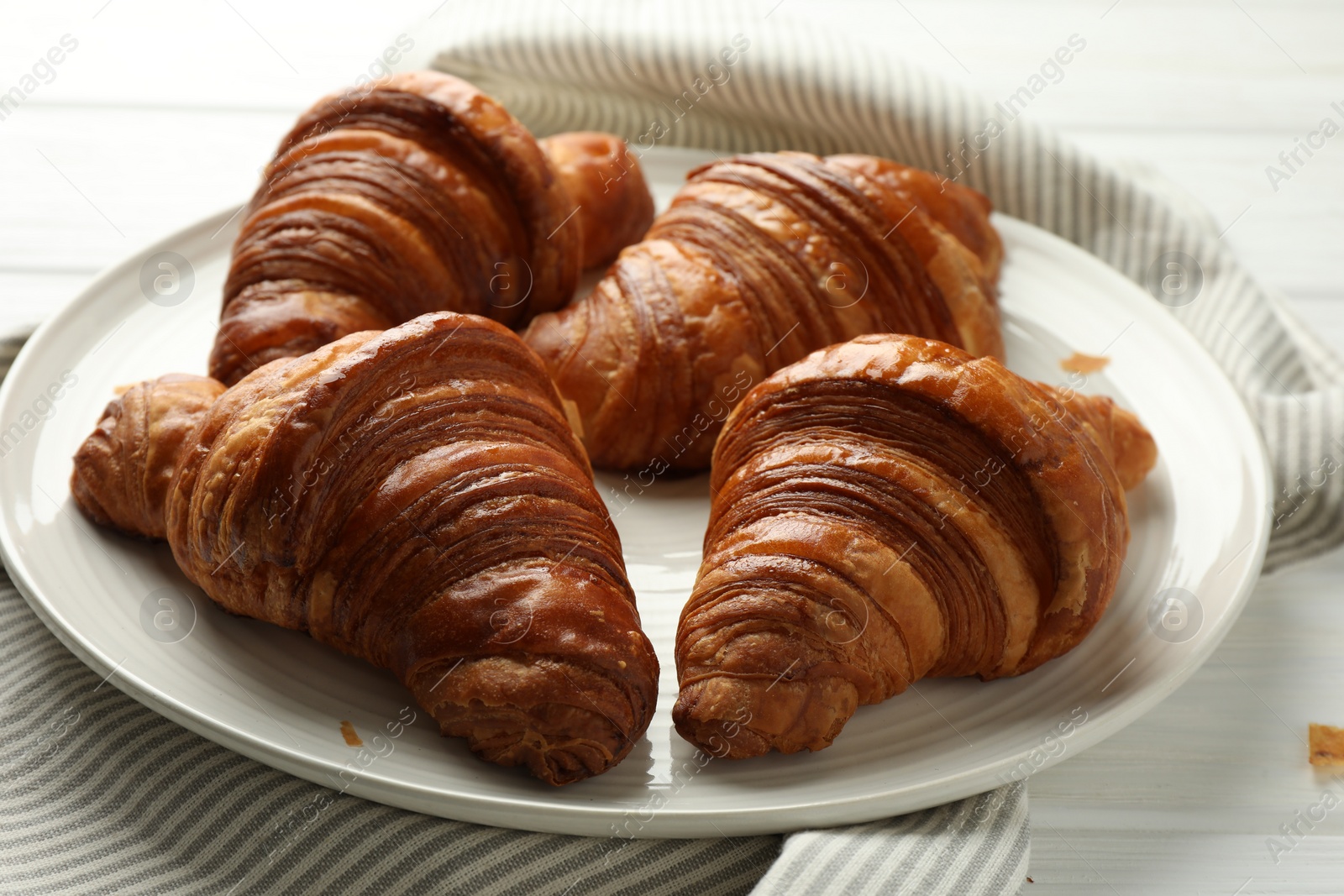 Photo of Plate with tasty croissants on white wooden table, closeup