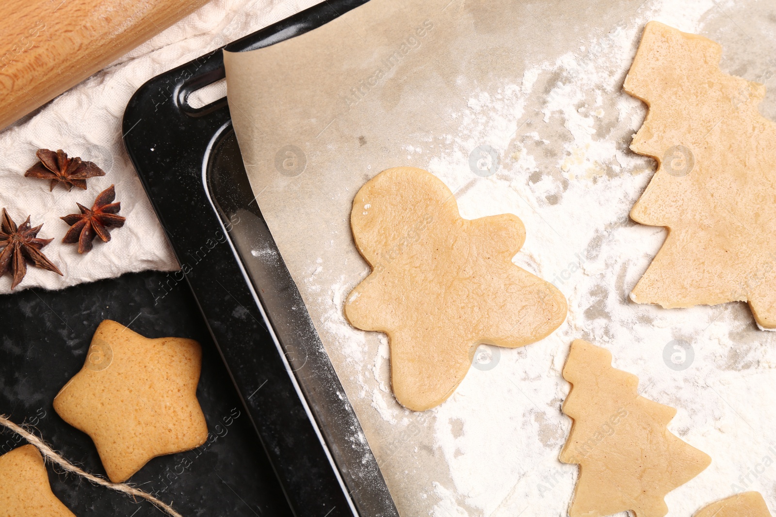 Photo of Raw Christmas cookies in baking tray and anise stars on table, flat lay