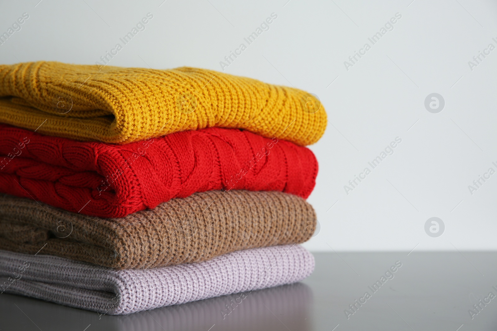 Photo of Stack of folded knitted sweaters on grey table