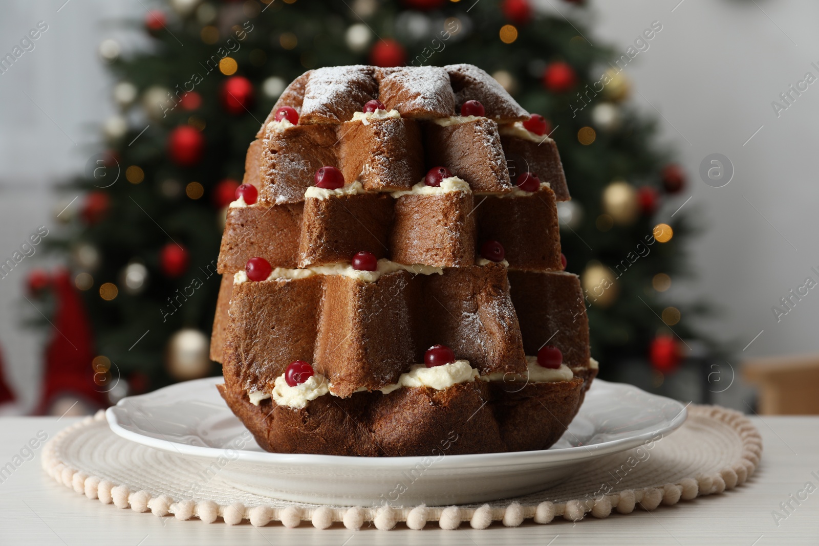 Photo of Delicious Pandoro Christmas tree cake with powdered sugar and berries on white table indoors