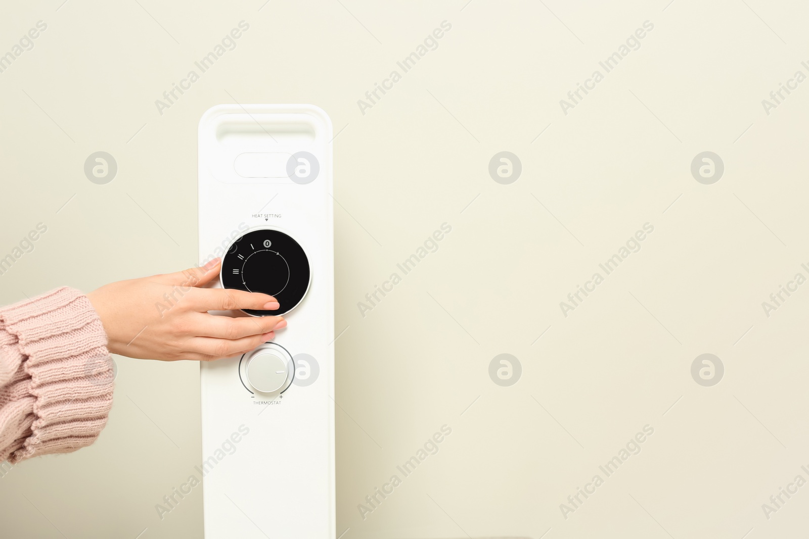 Photo of Young woman adjusting temperature on modern electric heater near beige wall, closeup. Space for text