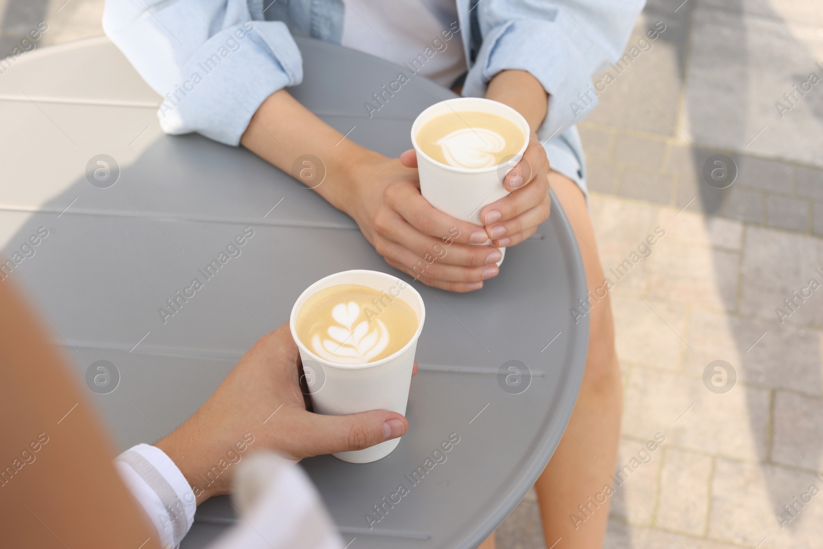 Photo of Coffee to go. Couple with paper cups at grey table outdoors, closeup. Space for text